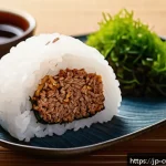 대체 단백질 요리법으로 만드는 영양 만점 주먹밥 - A close-up of a neatly shaped onigiri rice ball filled and mixed with textured soy meat, seasoned wi...